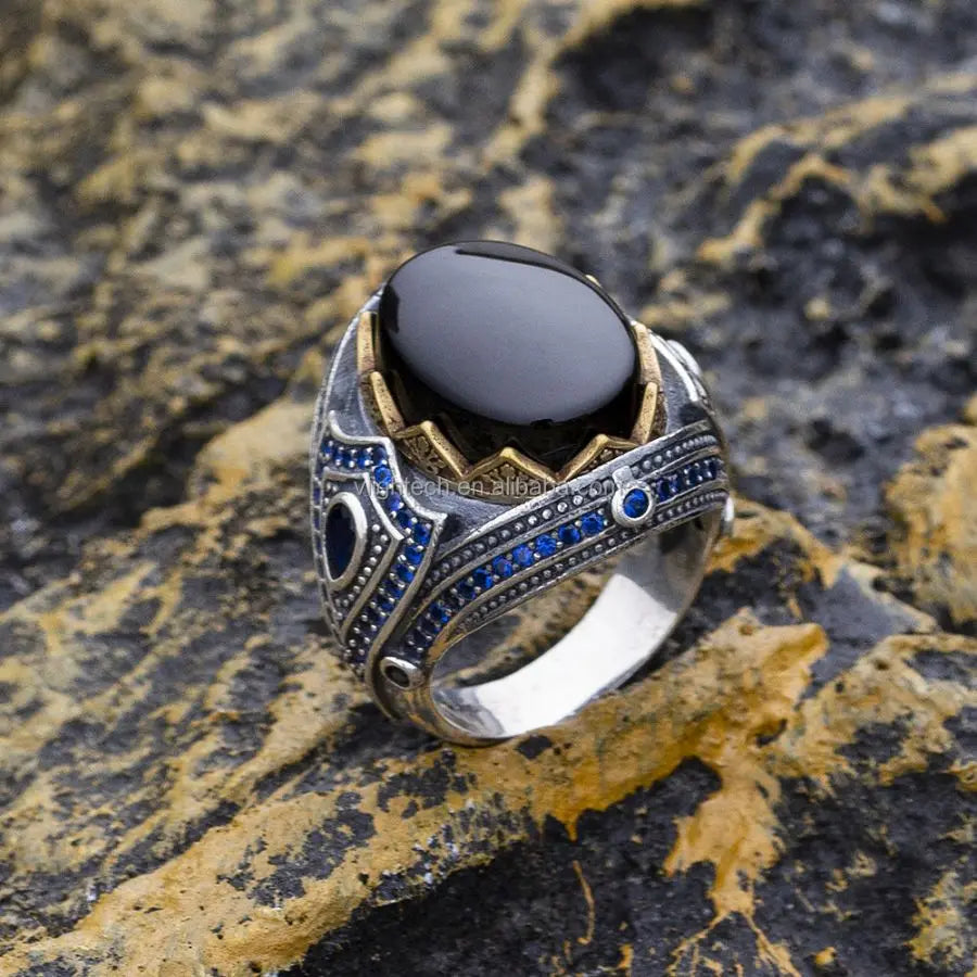 Decorative ring with black stone and blue accents on a textured stone surface