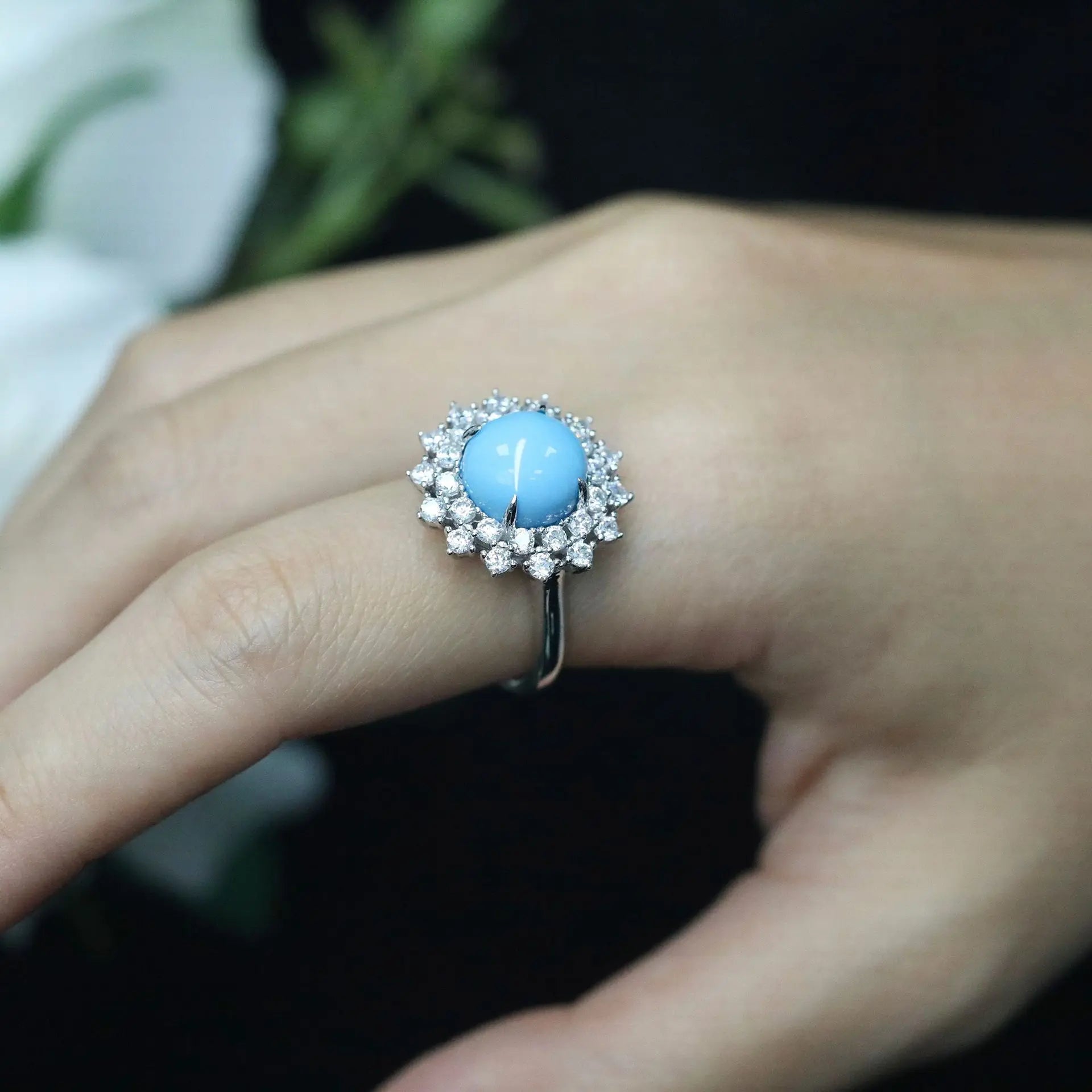 Ring with a blue gemstone and diamond-like stones on a finger against a blurred background