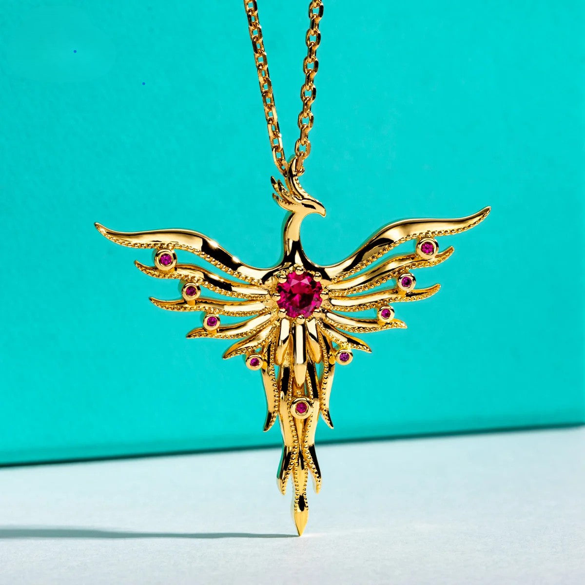 Gold phoenix necklace with red gemstones on a turquoise background