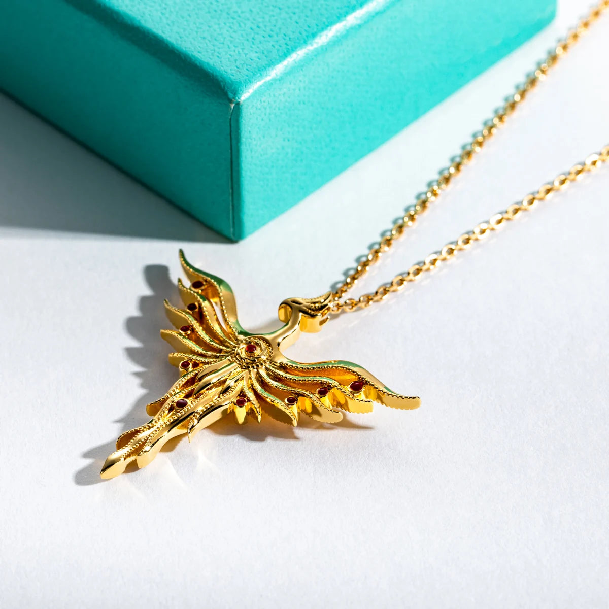 Gold dragon necklace on a white surface with a turquoise box in the background