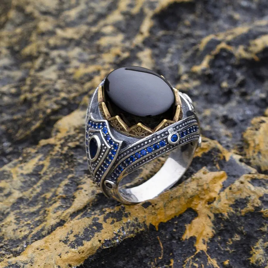 Silver ring with black stone and blue accents on a textured stone surface