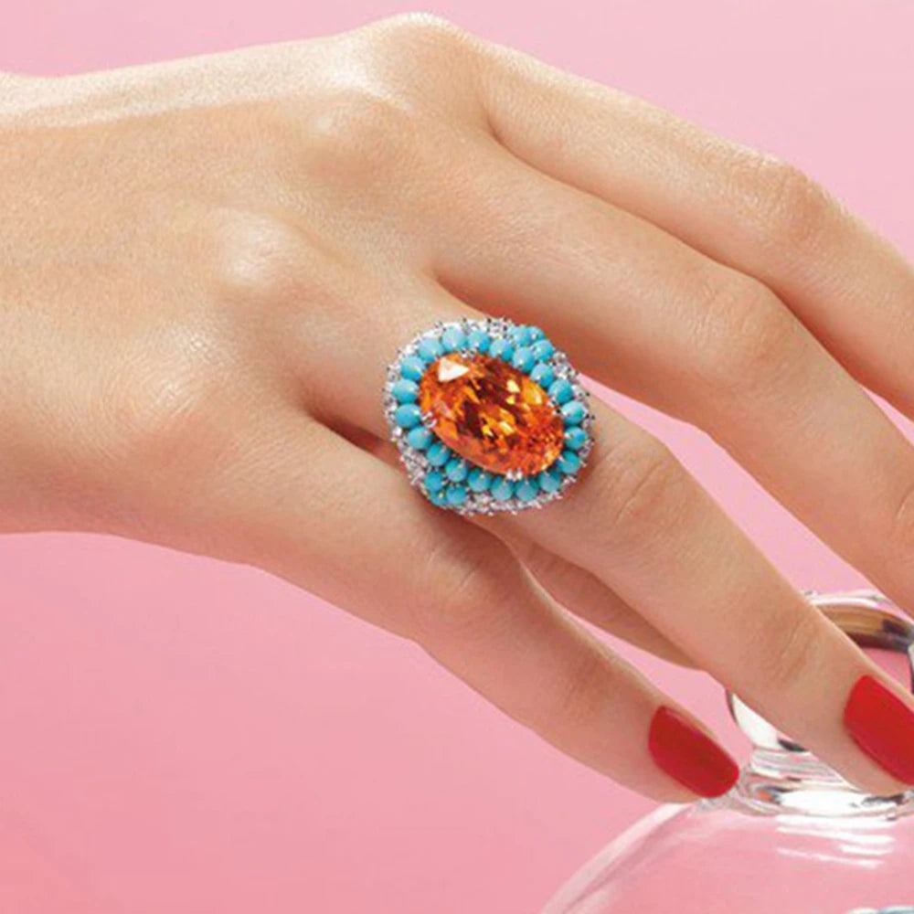 Ring with orange gemstone and turquoise accents on a hand against a pink background